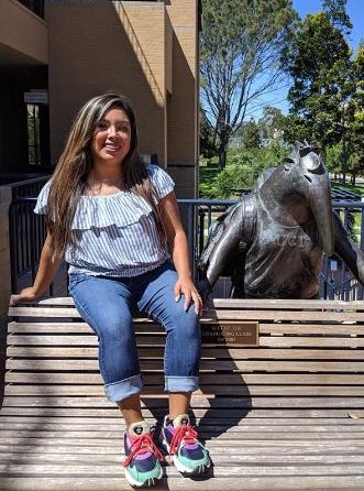 Photo of Ester Mendez sitting on steps smiling with long hair t-shirt and jeans